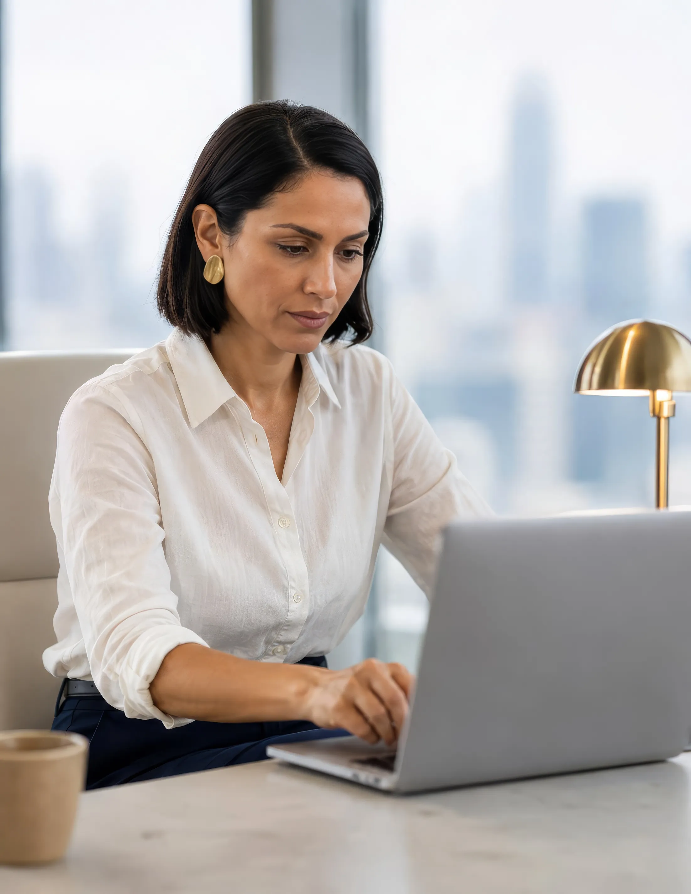 A woman working on her laptop at a desk overlooking a city skyline