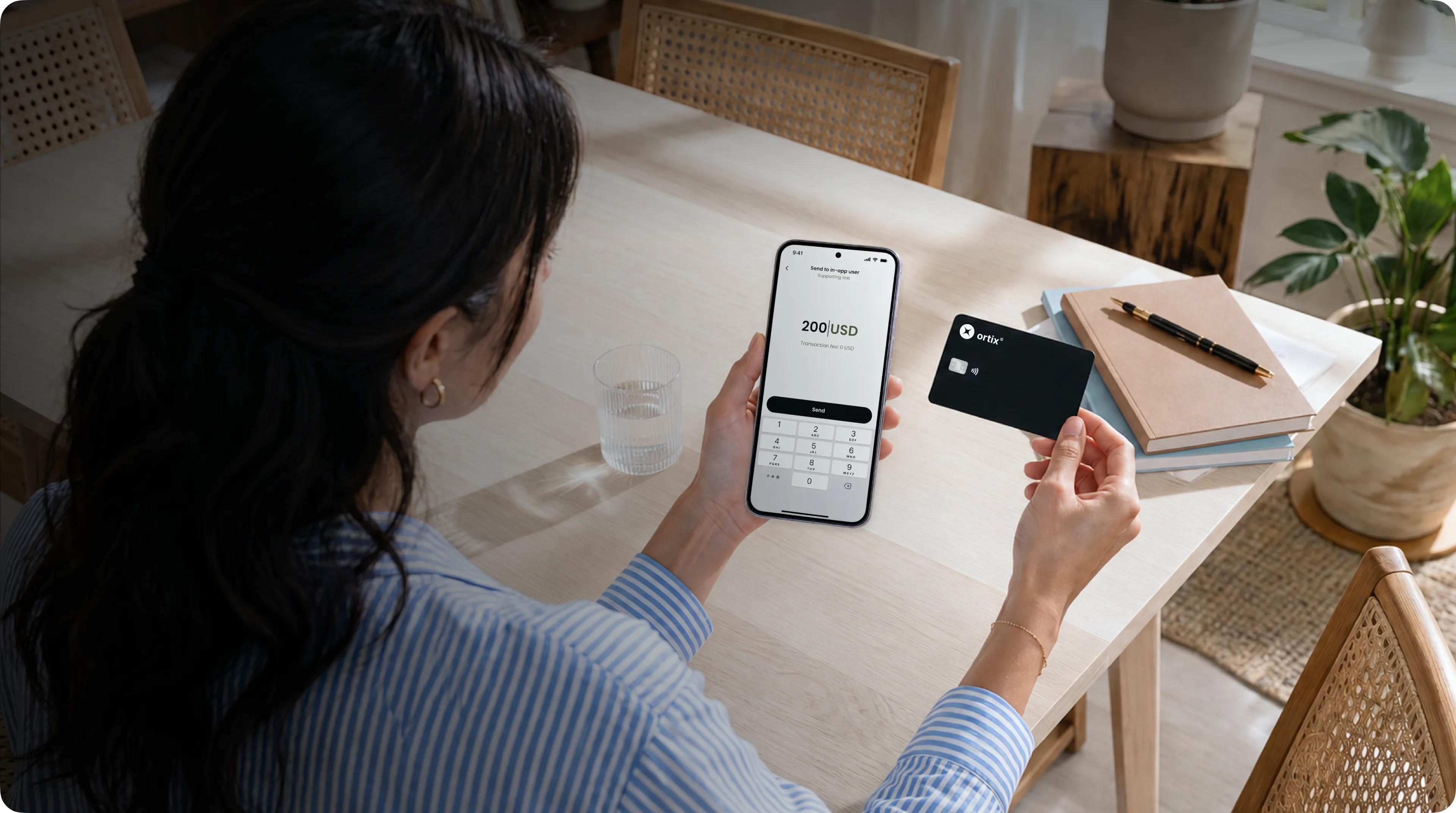 A woman sending money from her phone while holding an Ortix card at a table
